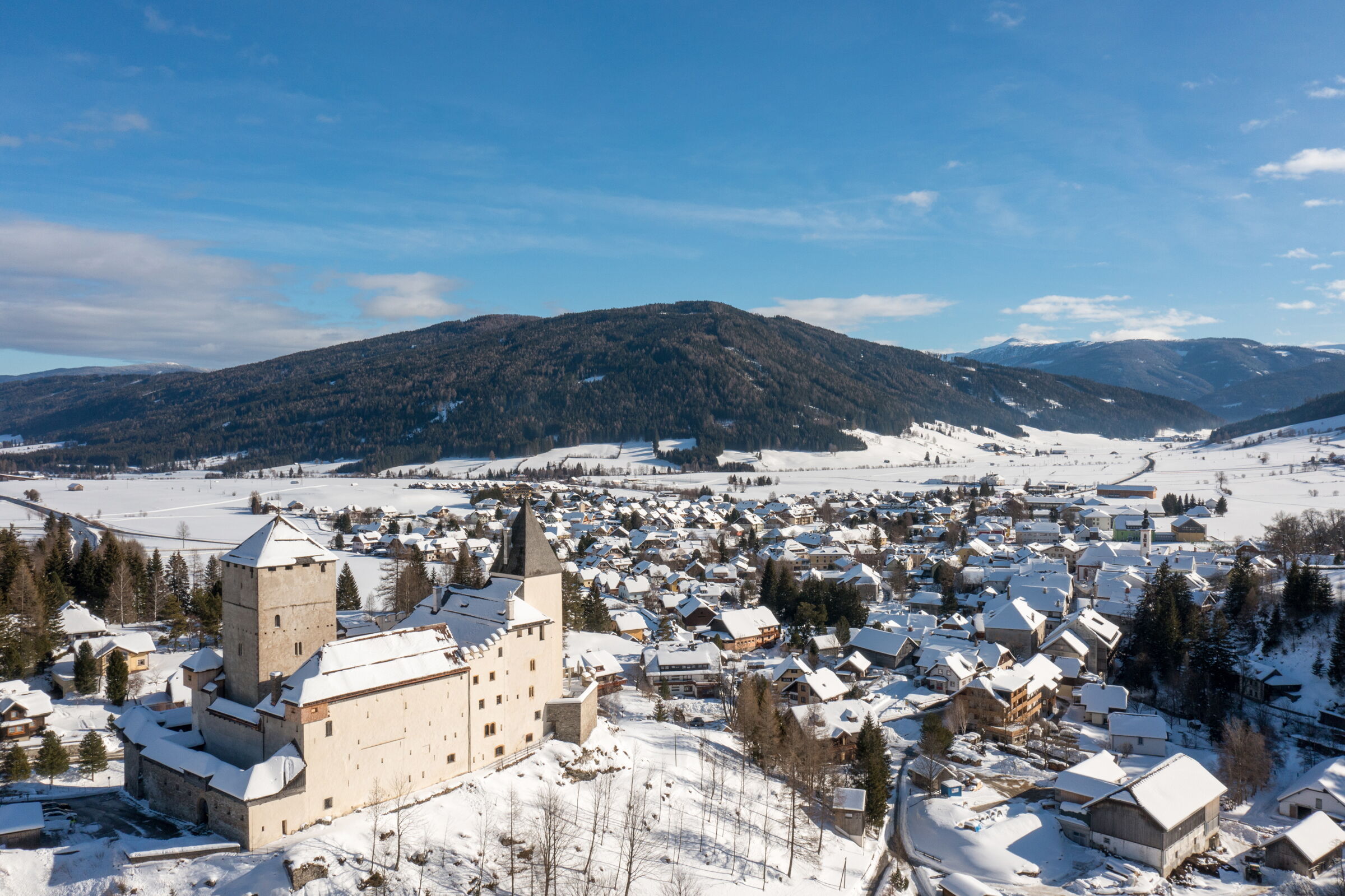 Snow-covered landscape with Mauterndorf Castle and surrounding village against a mountain backdrop.