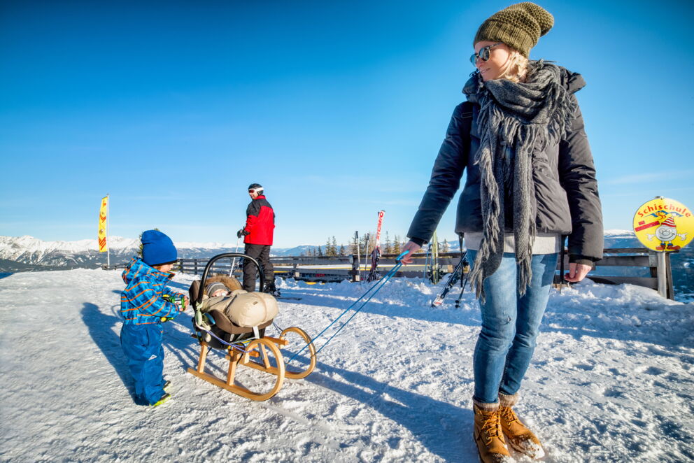 Familie genießt sonnigen Wintertag im Schnee mit Schlitten und herrlicher Aussicht.