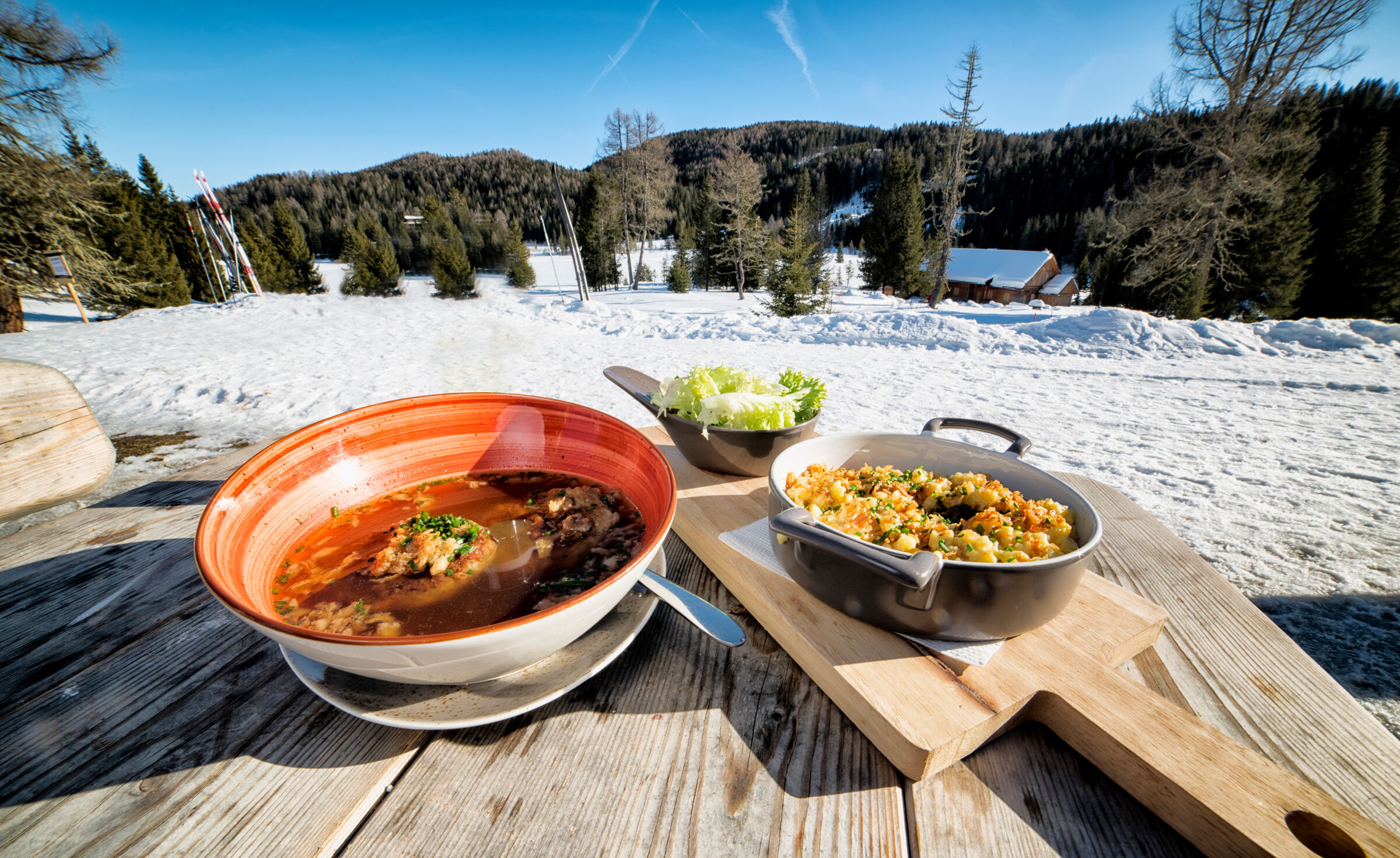 Schmackhafte Suppen auf Holztisch mit verschneiter Berglandschaft im Hintergrund.