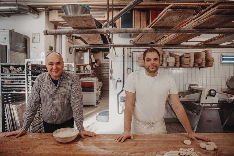 Zwei Bäcker in traditioneller Bäckerei, umgeben von Backutensilien und Teig.