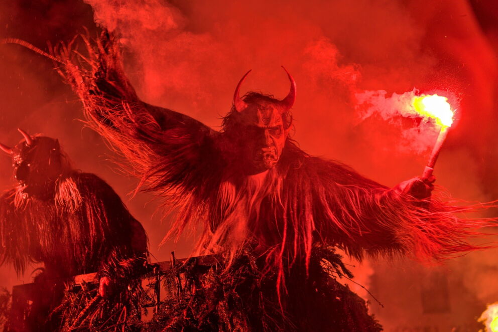 Personen in Krampuskostümen mit Fackel in dunkler, rauchiger Atmosphäre.