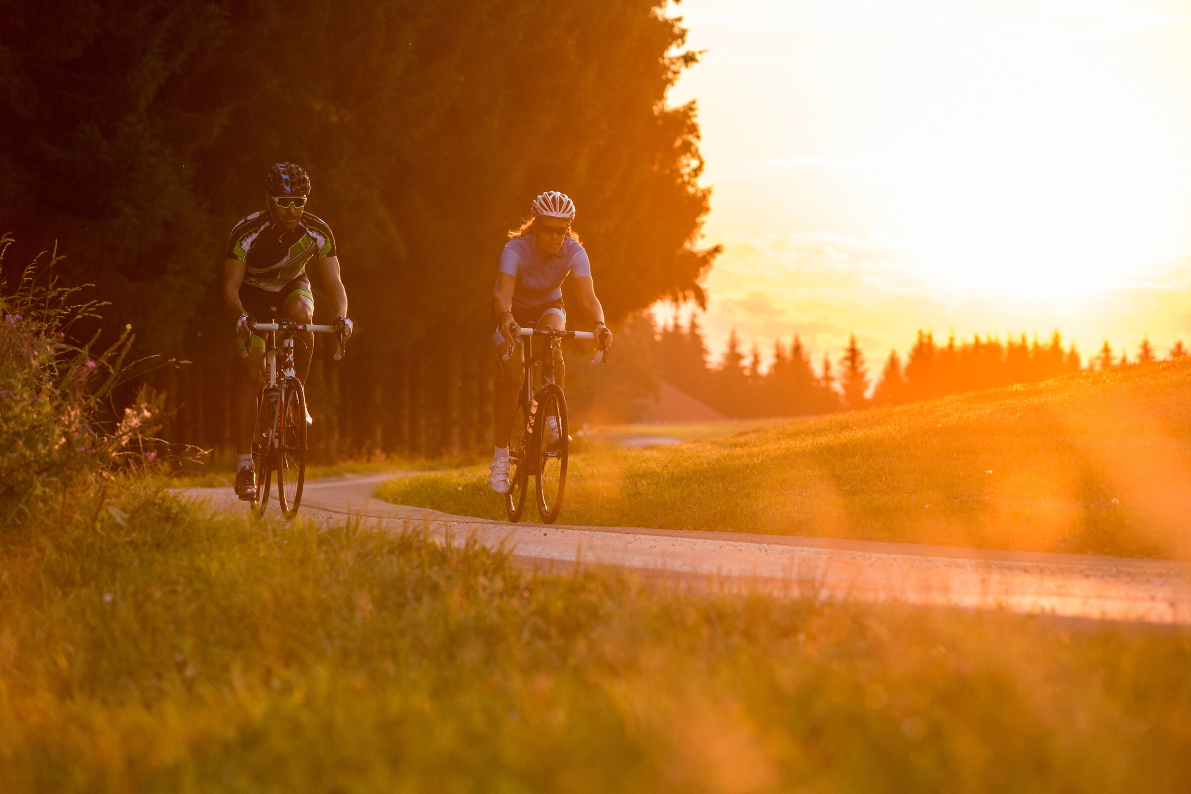 Zwei Radfahrer bei Sonnenuntergang auf einer idyllischen Landstraße in der Natur.