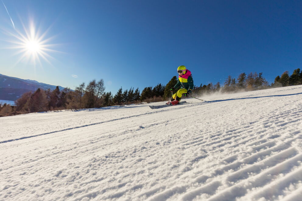 Skifahrer gleitet schwungvoll die Piste hinunter bei klarem Sonnenschein und blauem Himmel.