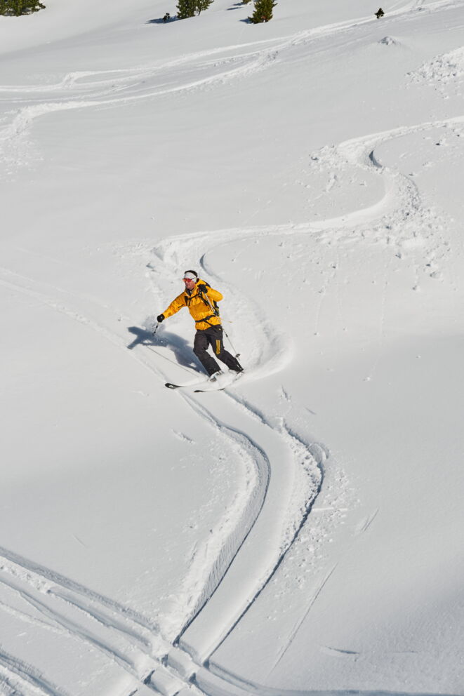 Skifahrer zieht Schwünge im frischen Pulverschnee bei strahlendem Sonnenschein.