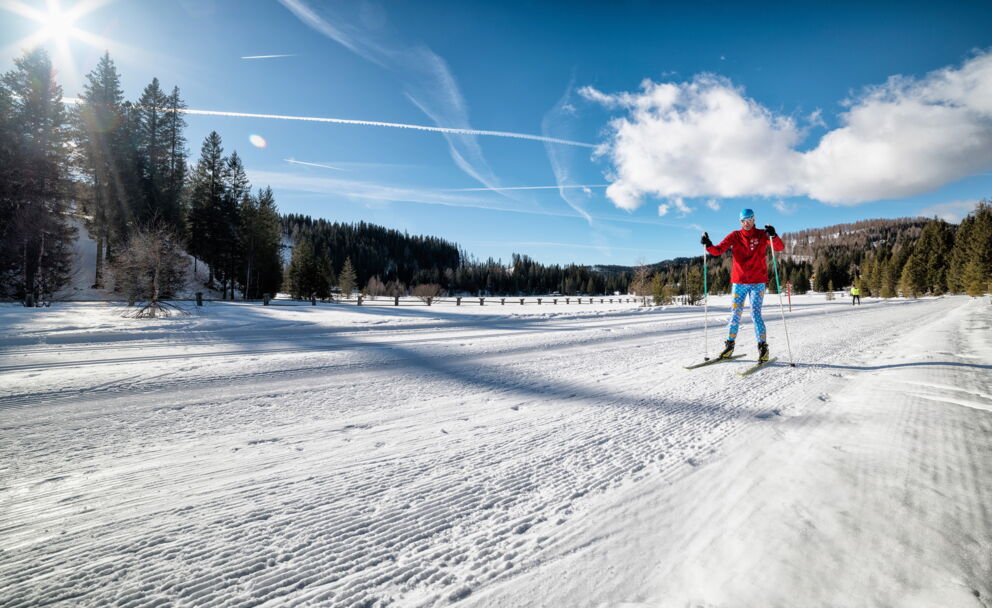 Skifahrer auf präparierter Piste unter strahlend blauem Himmel und Sonnenschein.