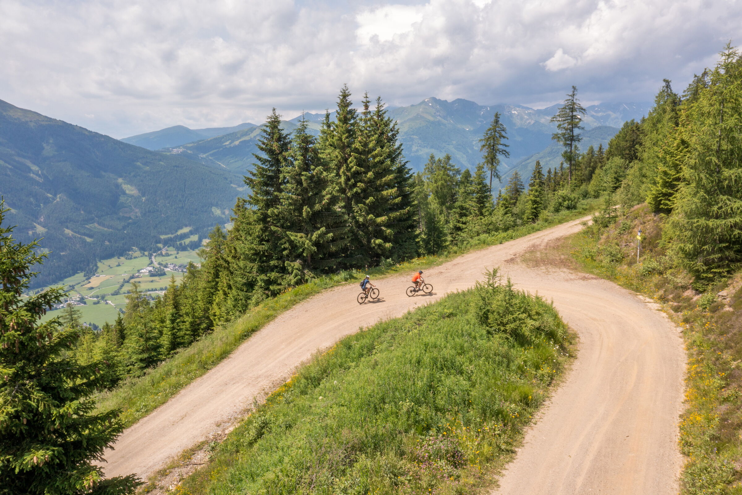 Zwei Radfahrer auf kurviger Bergstraße mit beeindruckendem Talblick und dichten Wäldern.