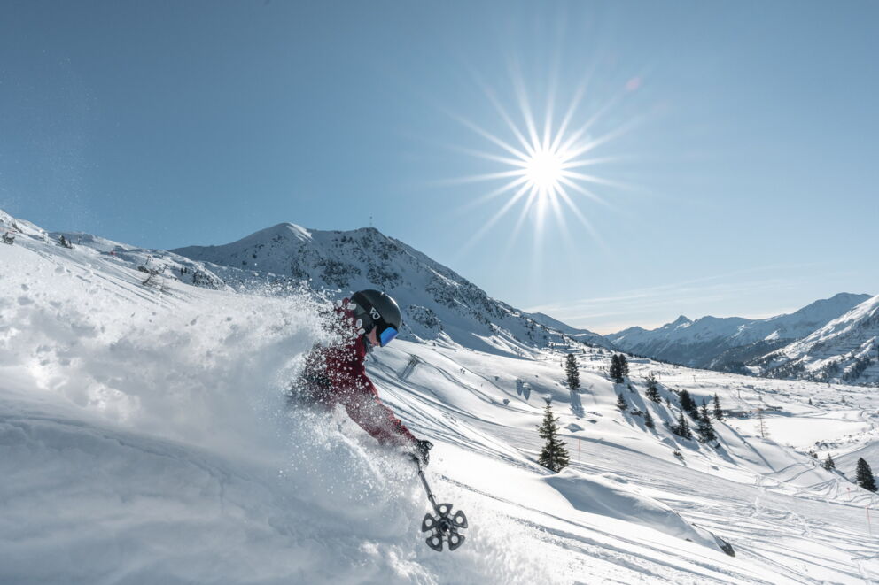 Skifahrer in actionreicher Abfahrt auf schneebedecktem Berg unter strahlender Sonne.
