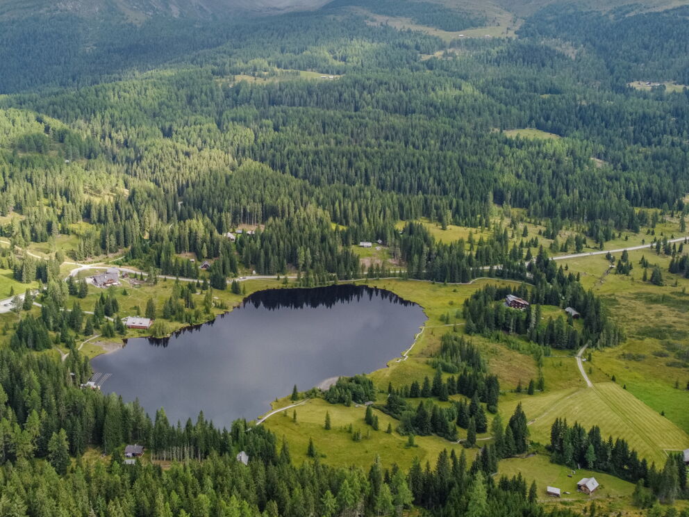 Waldumgebener Bergsee in idyllischer Landschaft mit kleinen Gebäuden und Wegen